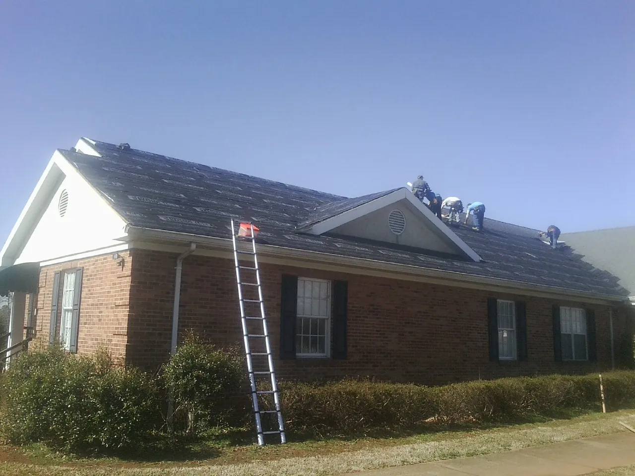 Crew tearing shingles off a brick ranch roof with a ladder set — Metal Roof Repair work by our crew in Cookeville