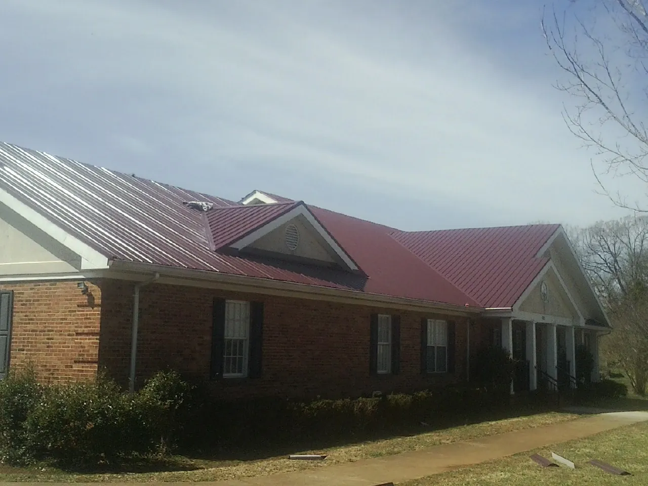Red metal roof with gabled entries on a long brick building, from a Hail Damage Roof Repair job in Cookeville