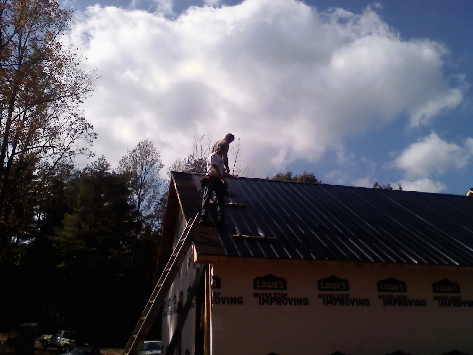 Roofer fastening dark metal panels high against a cloudy sky, from a Roof Inspection job in Cookeville