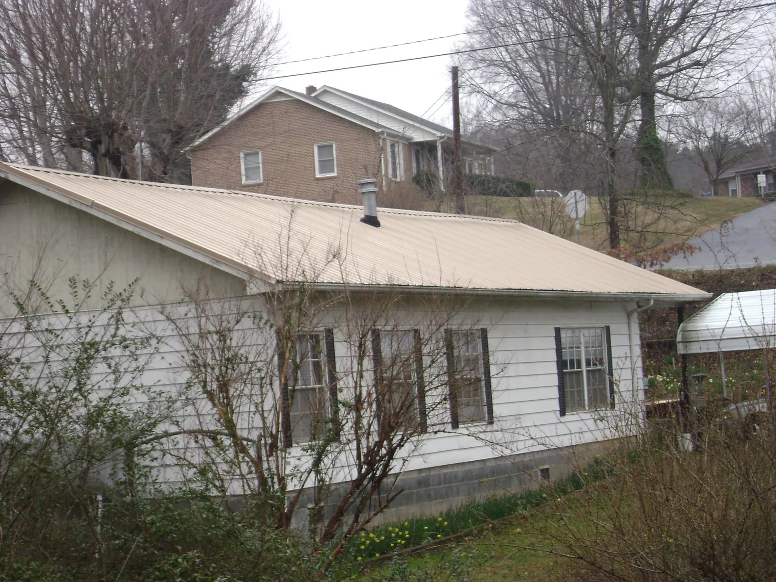 Tan metal roof on a white sided house set into a hillside — Commercial Roofing by Roofing Brothers in Cookeville